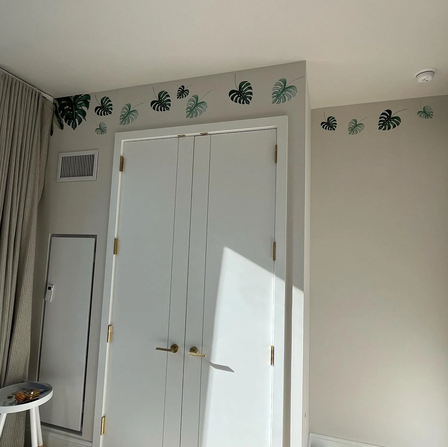 Nursery closet doors framed by monstera leaf decals at the crown