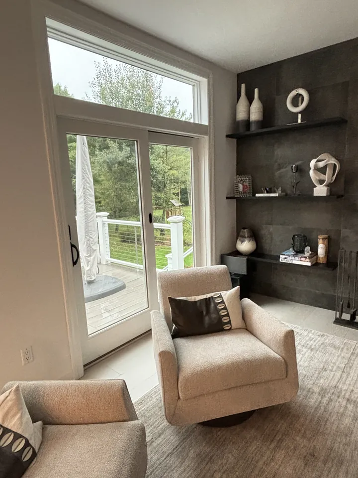 Dark accent wall with floating shelves and beige swivel chair by the terrace doors