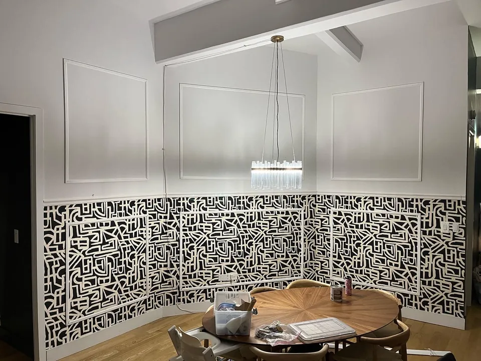 Bathroom vanity against black and white monogram wallpaper with sconce lighting