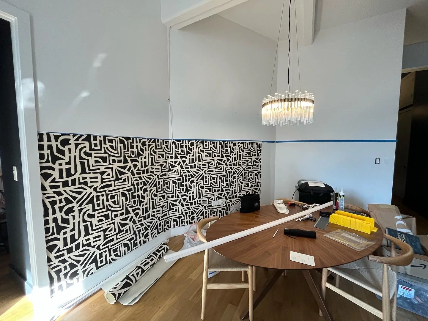 Dining room with bold tribal monogram wallpaper below the chair rail and crystal chandelier