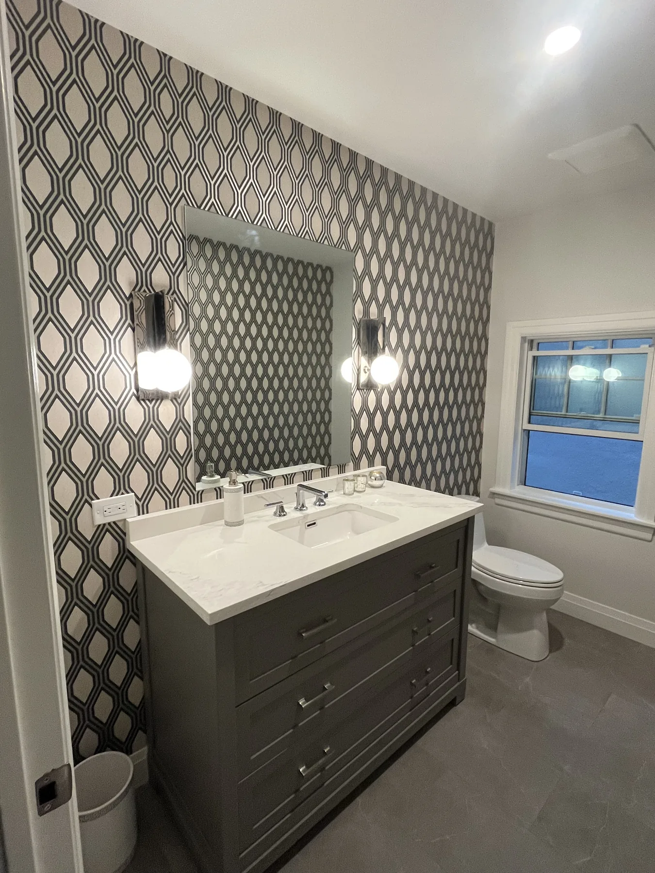 Powder room with ogee patterned wallpaper and dark vanity by Flat Arq